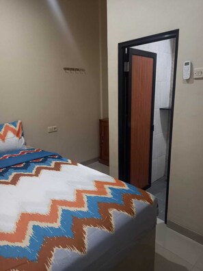 Habitació d'hotel amb un llit, una porta que condueix a un bany i un termòstat fixat a la paret.