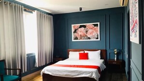 A bedroom with a wooden bed, white bedding, a red pillow, a floral painting on the wall, and a window with curtains. - Phuong Thuy Hotel Thu Duc near QL13 (Ho Chi Minh City)