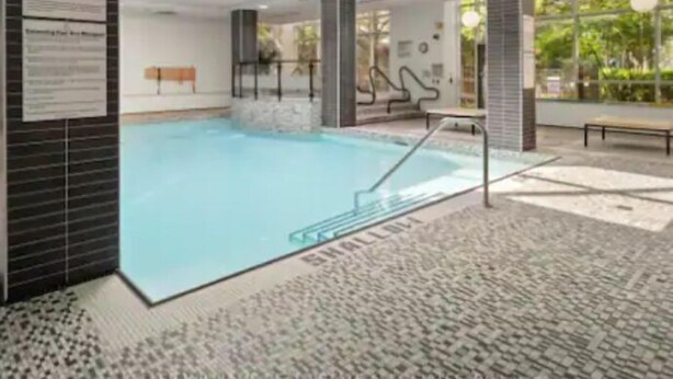 A modern indoor swimming pool with a clear view of the pool area, a bench, and a wall with informational posters.