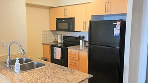 A kitchen with granite countertops, a stainless steel sink, a black refrigerator, and wooden cabinets.