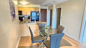 A modern kitchen with a dining area, featuring a glass table and chairs, wooden cabinets, and a refrigerator.
