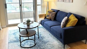 A living room with a blue sofa, a round coffee table, and a view of a cityscape through large windows.