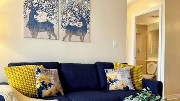 Una sala moderna con un sofá azul oscuro, cojines amarillos y estampados, una mesa redonda de centro con objetos decorativos y dos obras de arte murales que representan ciervos.