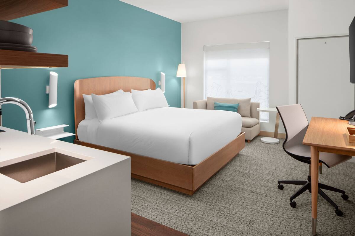 A modern hotel room with a large bed, a desk, and a chair.