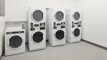 A row of four white front-loading washing machines in a clean, empty room with a plain white wall and a light-colored floor.