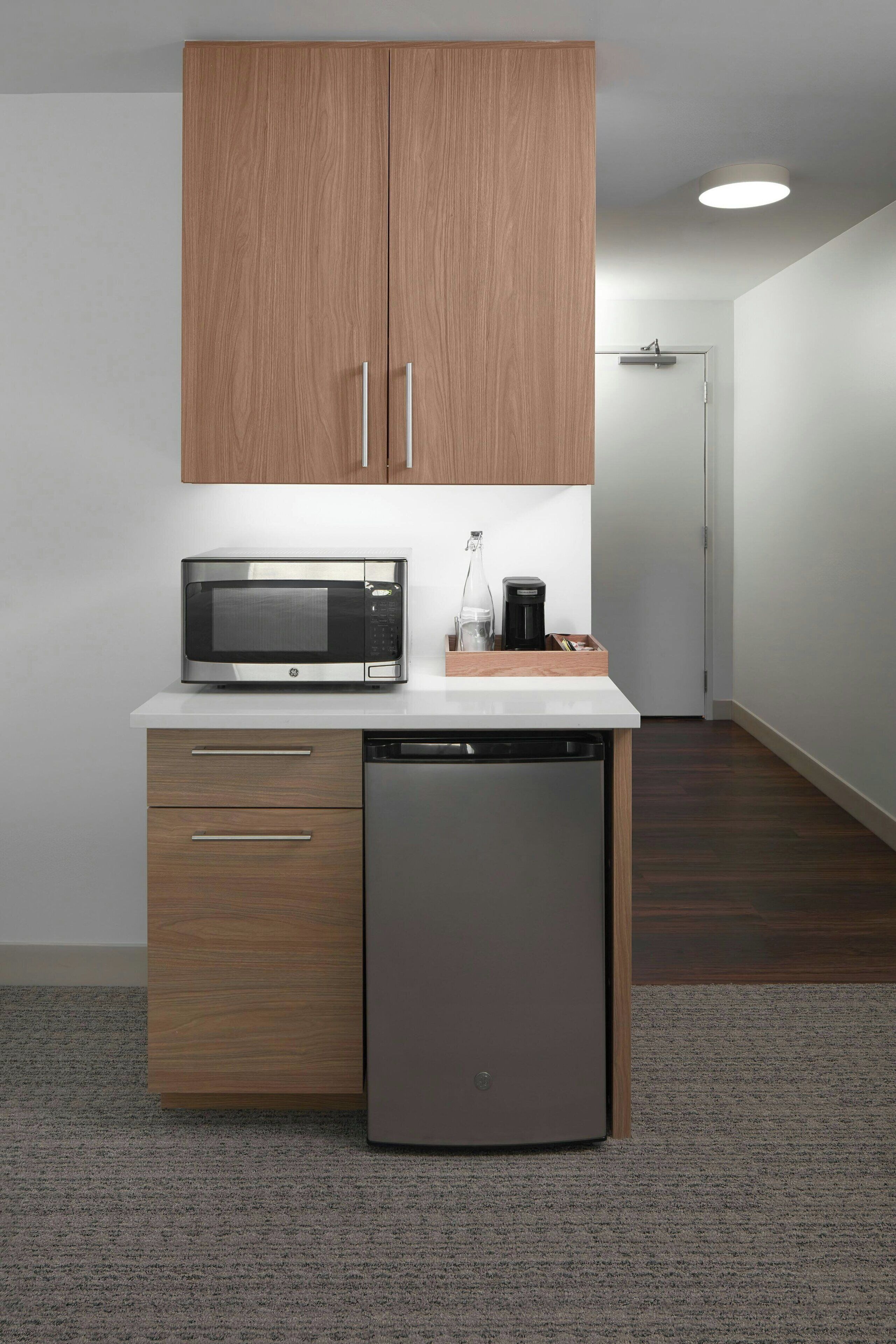Uma cozinha compacta com armários de madeira, micro-ondas, cafeteira e máquina de lavar louça.
