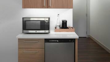 Uma cozinha compacta com armários de madeira, micro-ondas, cafeteira e máquina de lavar louça.