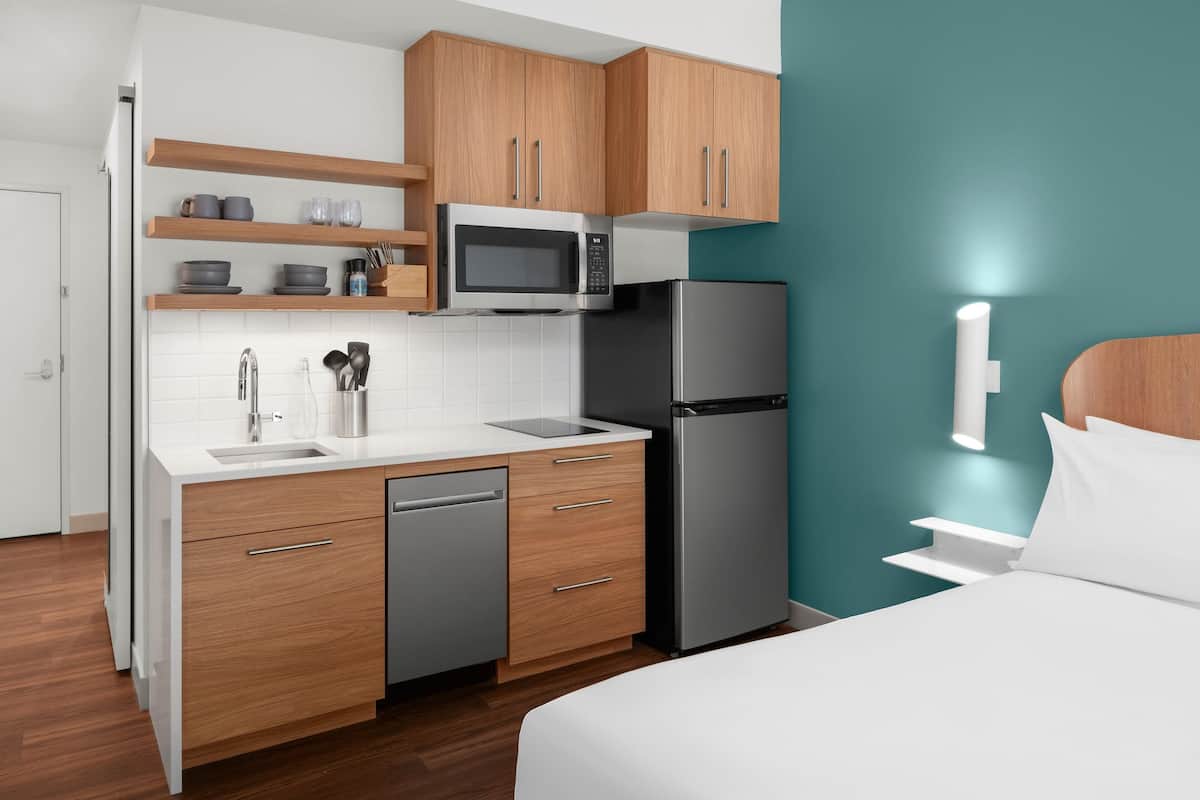 A compact kitchen with wooden cabinets, a microwave, a refrigerator, and a dishwasher.