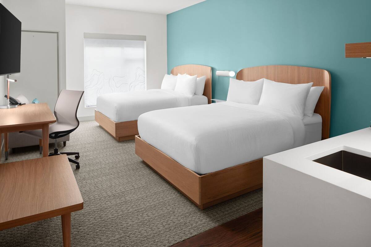 A hotel room with two beds, a desk, a chair, and a TV.