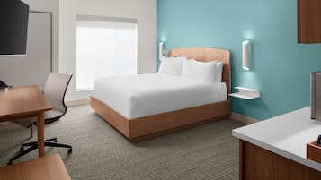 A modern hotel room with a large bed, a desk, a chair, a TV, and a window with a view.