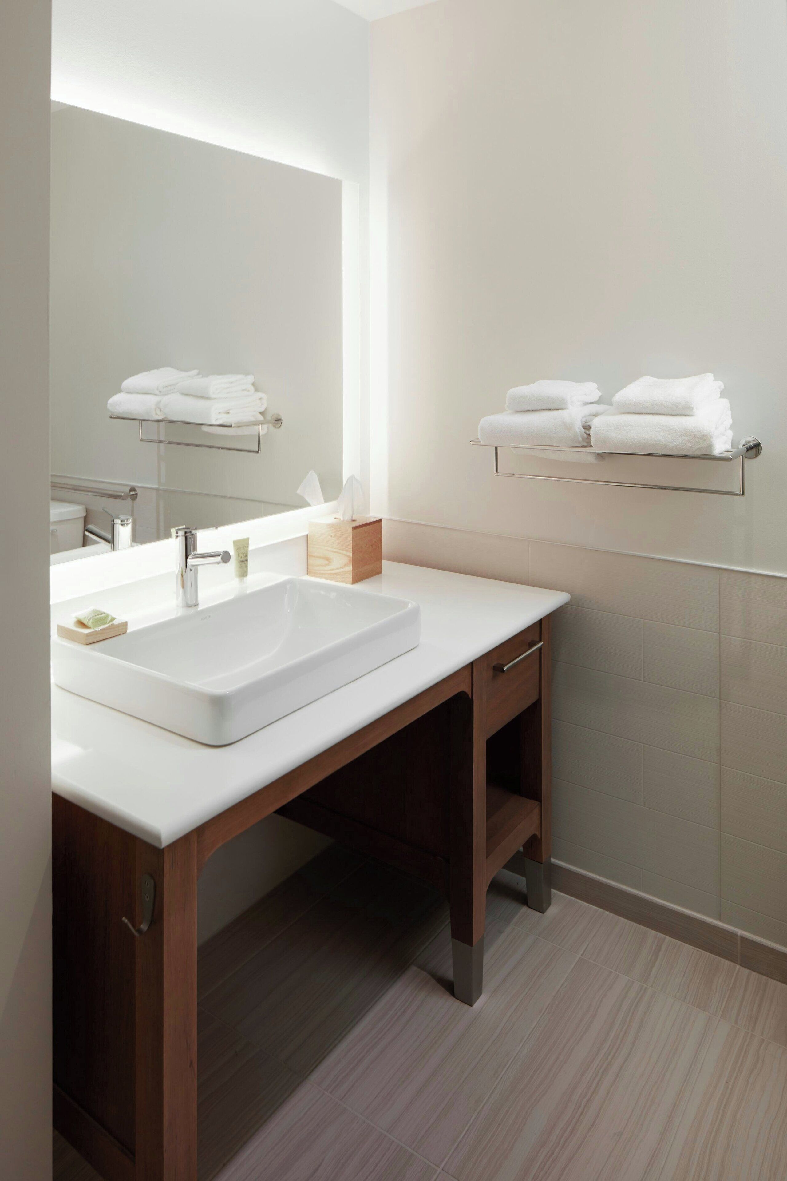 A modern bathroom with a white sink, wooden vanity, and towel racks on the wall.
