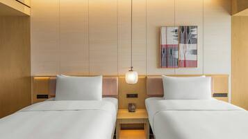 A hotel room with two beds, a bedside table with a lamp, a phone, and a wall-mounted artwork.