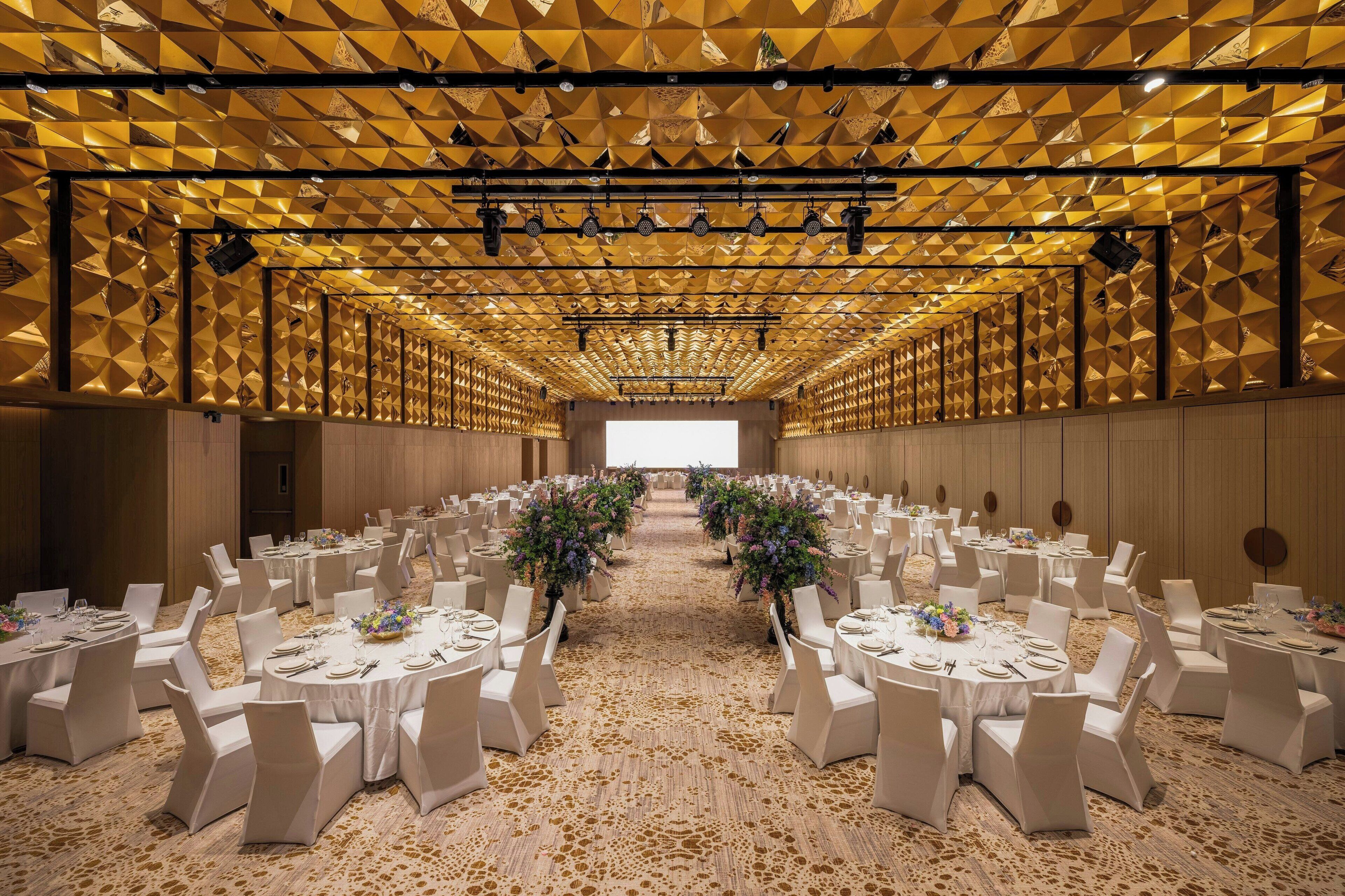 A banquet hall with round tables, white chairs, and floral centerpieces.
