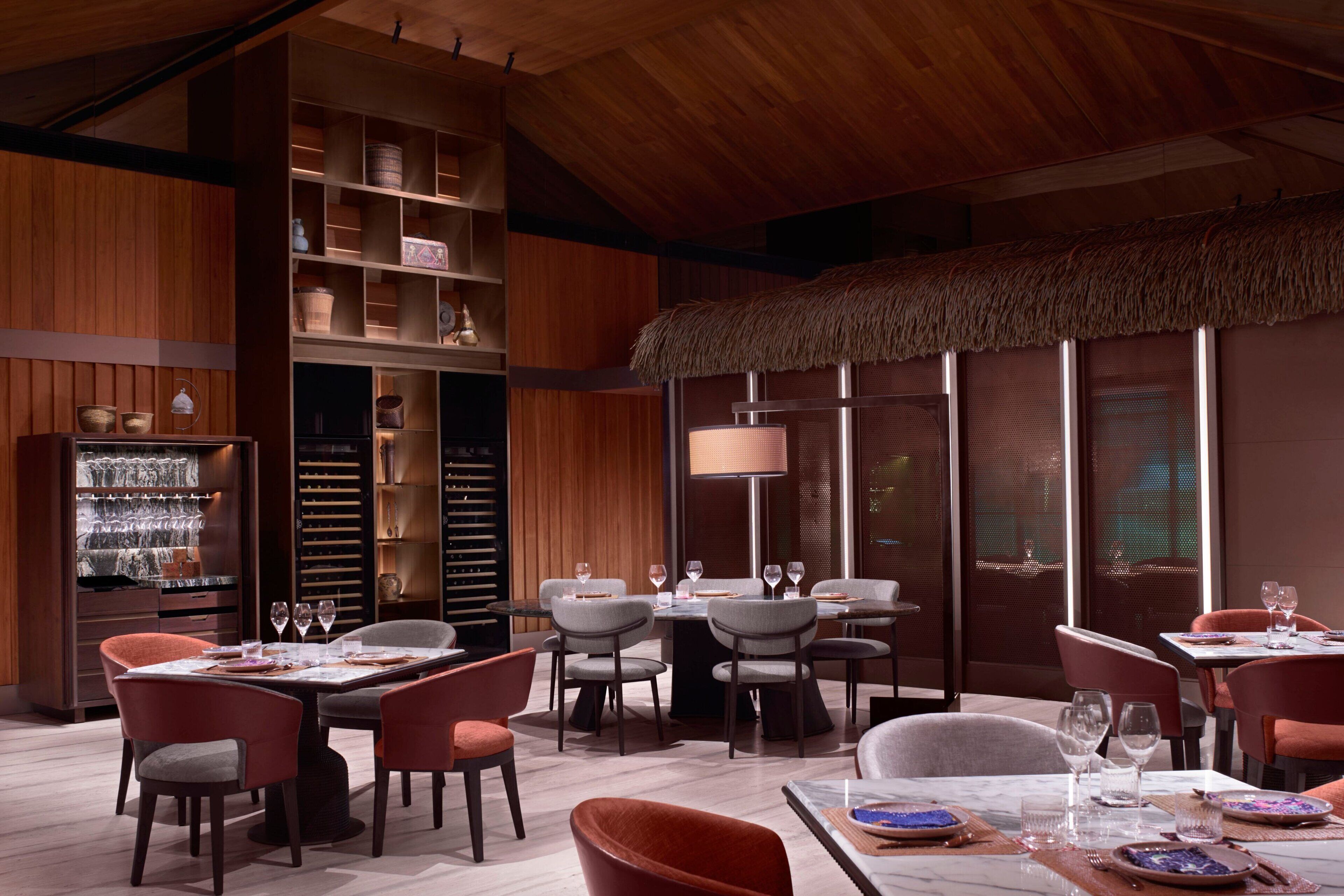A restaurant with multiple dining tables and chairs, a large window with a view, and a wooden ceiling.
