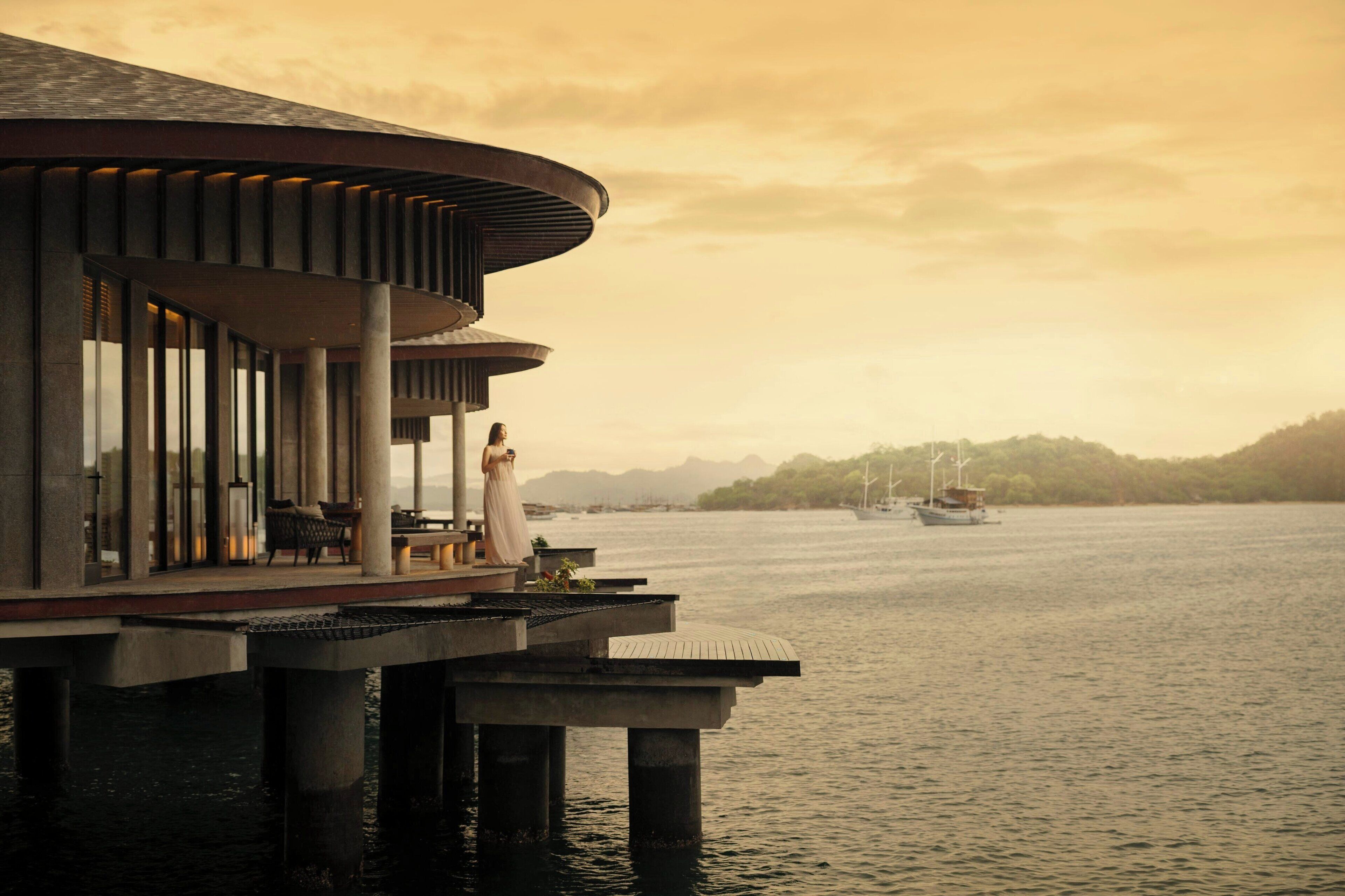 A waterfront hotel with a modern design, featuring a balcony with seating and a view of the water.