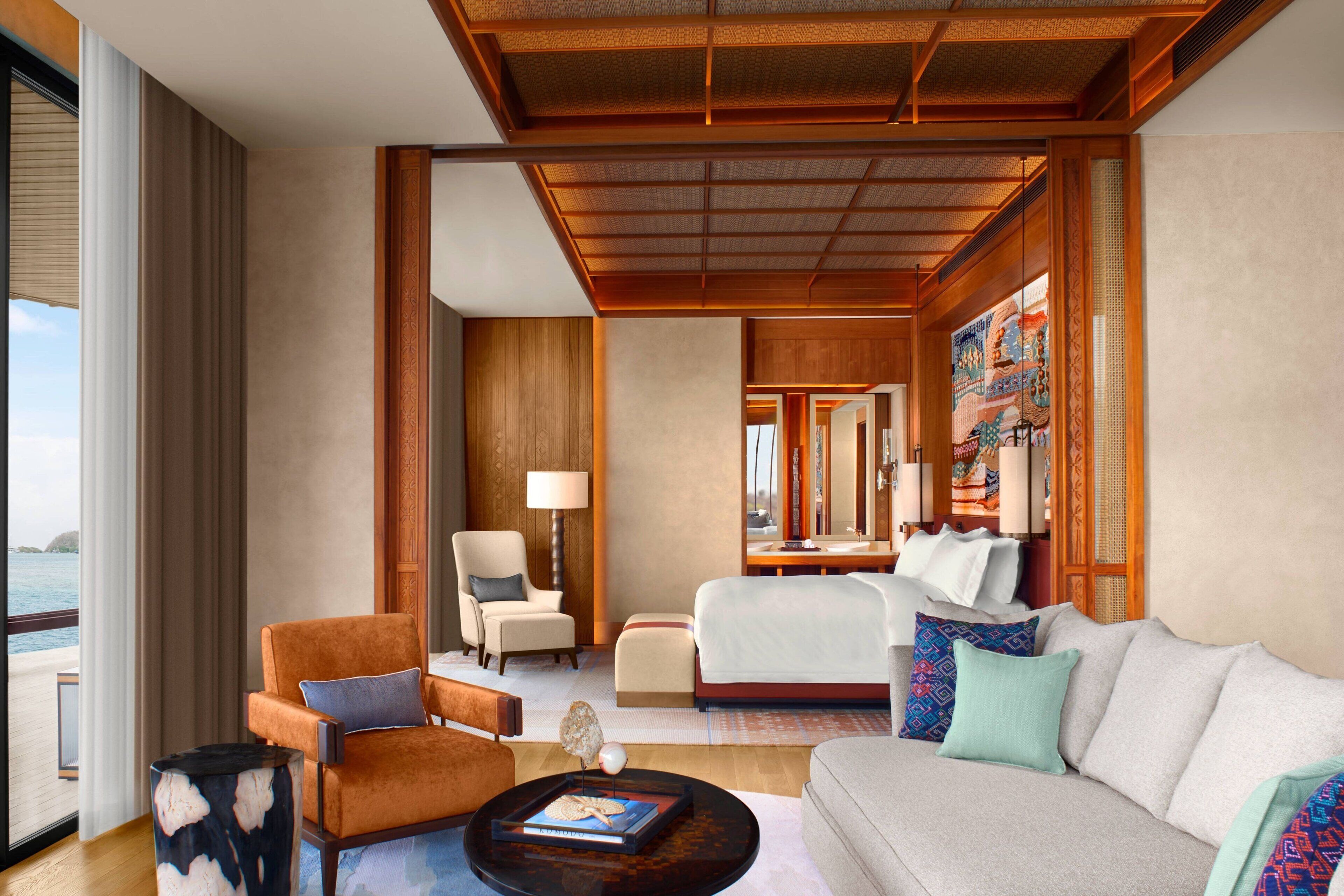 A hotel room with a large bed, a sofa, a chair, a coffee table, and a view of the sea.