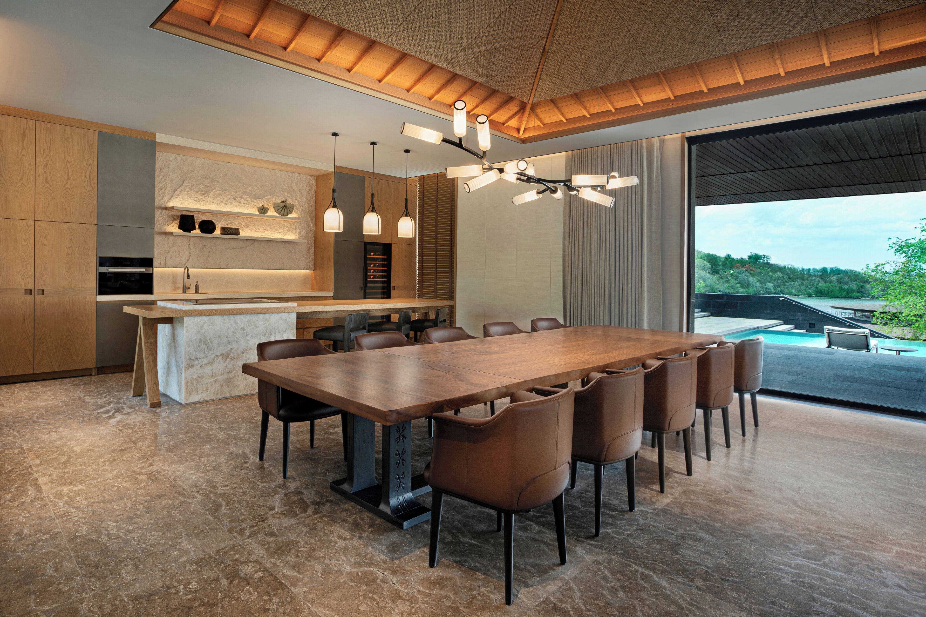Una cocina moderna con una isla central, iluminación colgante y una amplia mesa de comedor con sillas.