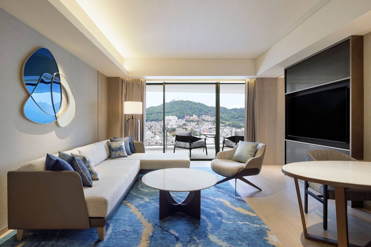 Een moderne hotelkamer met een groot raam, een bank, een ronde salontafel en een televisie.