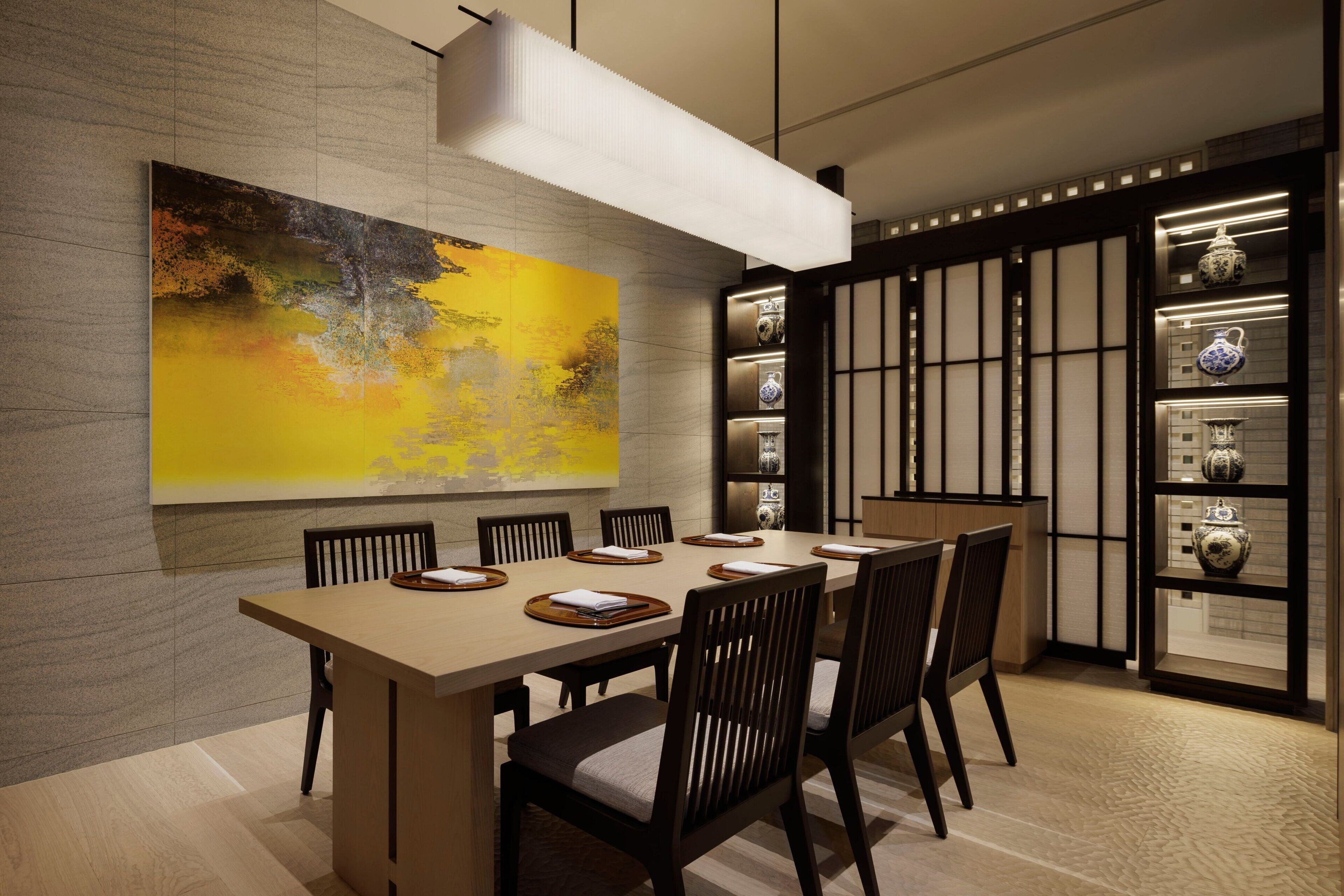 Un espace de salle à manger moderne, avec une longue table, des chaises et un grand tableau abstrait accroché au mur.