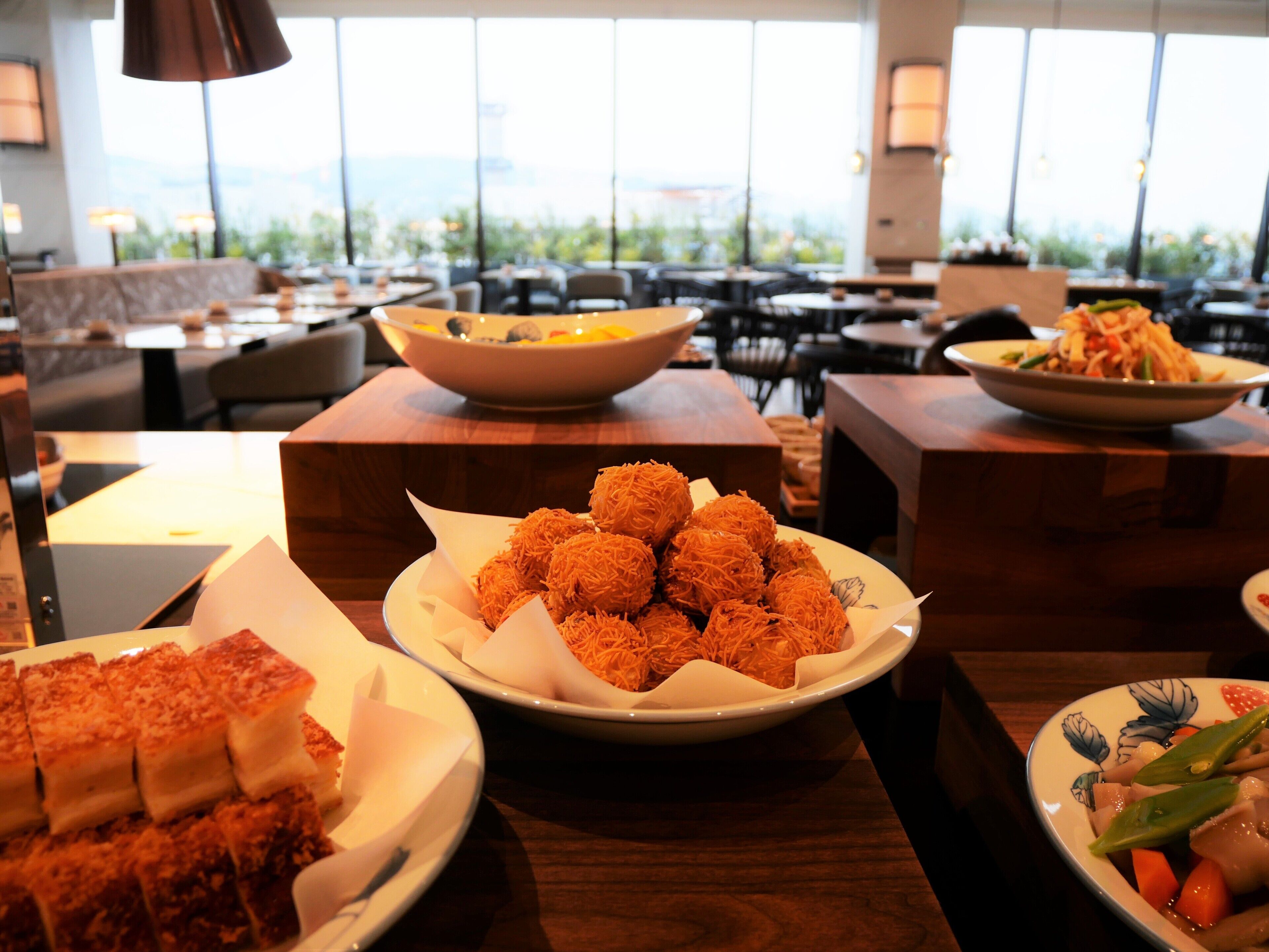Un restaurante con varias mesas y sillas, un tazón grande de comida y platos de comida en primer plano.