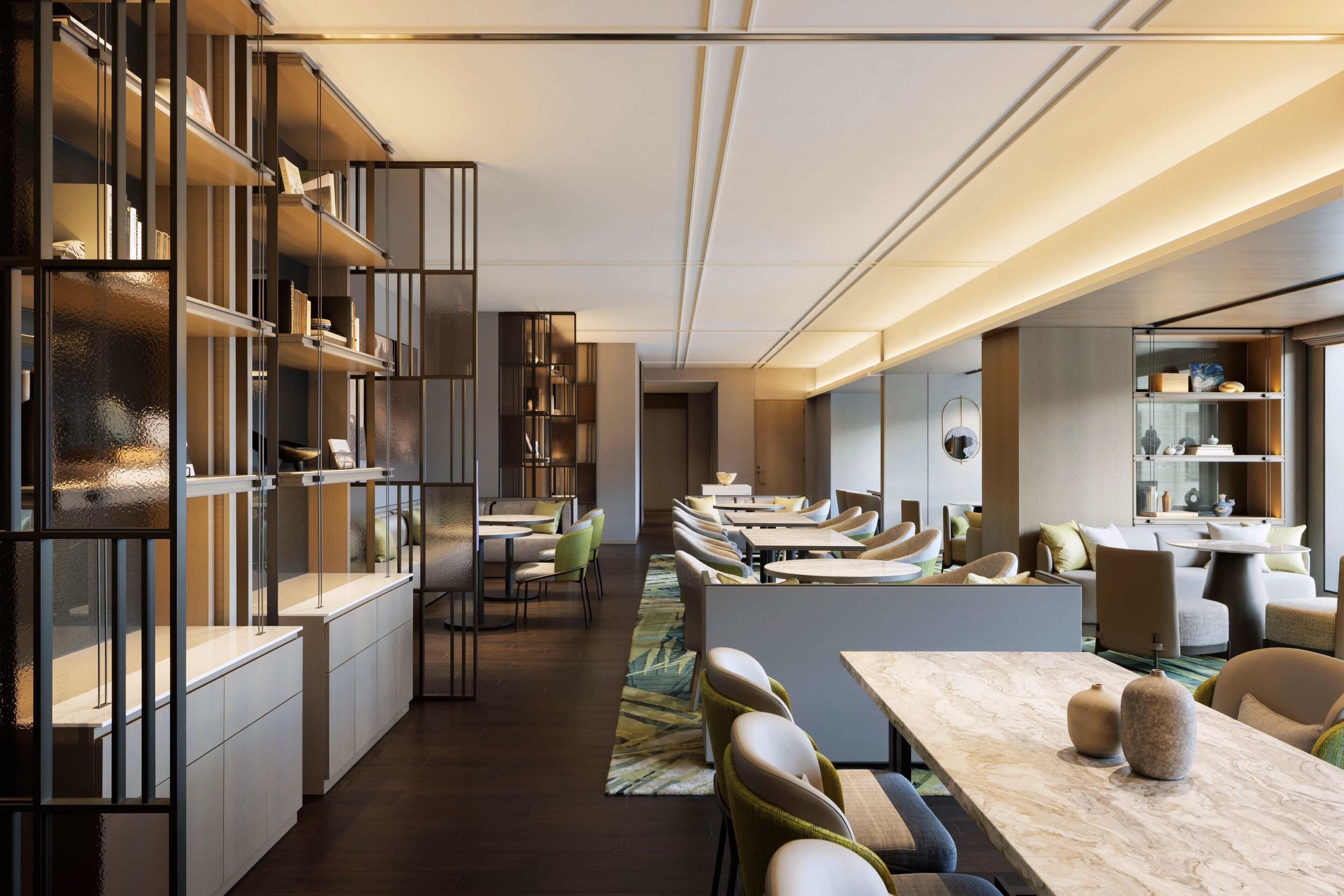 A modern hotel lobby with a long reception desk, seating area, and a large bookshelf.