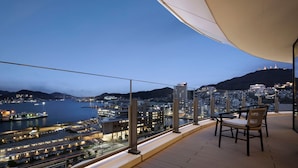 Un balcon offrant une vue sur un paysage urbain et une étendue d’eau au crépuscule.