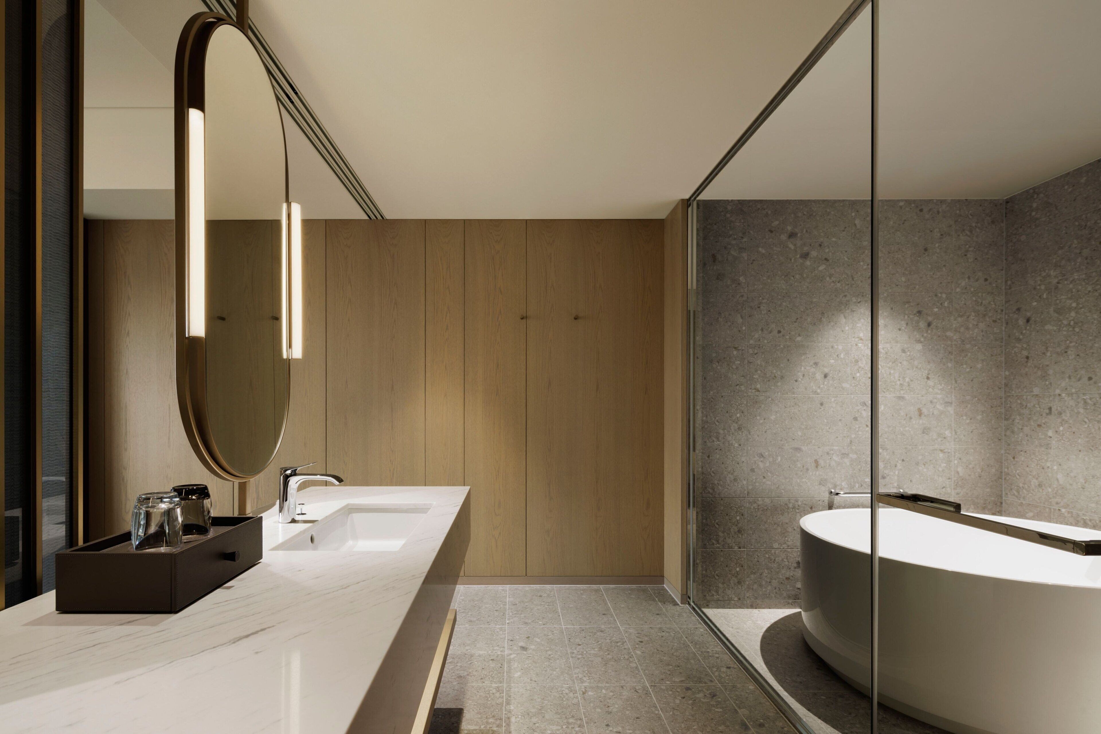 A modern bathroom with a large mirror, a wooden vanity, a freestanding bathtub, and a glass shower enclosure.