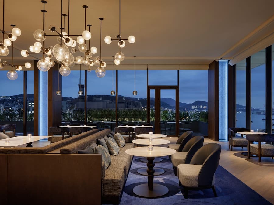 A modern dining area with round tables and comfortable seating, large windows offering a city view.