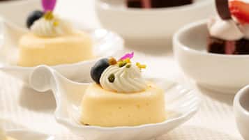 Presentación de postre con un dulce amarillo cremoso cubierto de crema batida y bayas, servido en un tazón blanco.