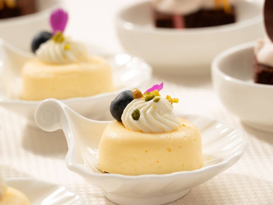 Presentación de postre con un dulce amarillo cremoso cubierto de crema batida y bayas, servido en un tazón blanco.