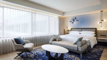 A hotel room with a large bed, a sofa, a small table, and a chair.