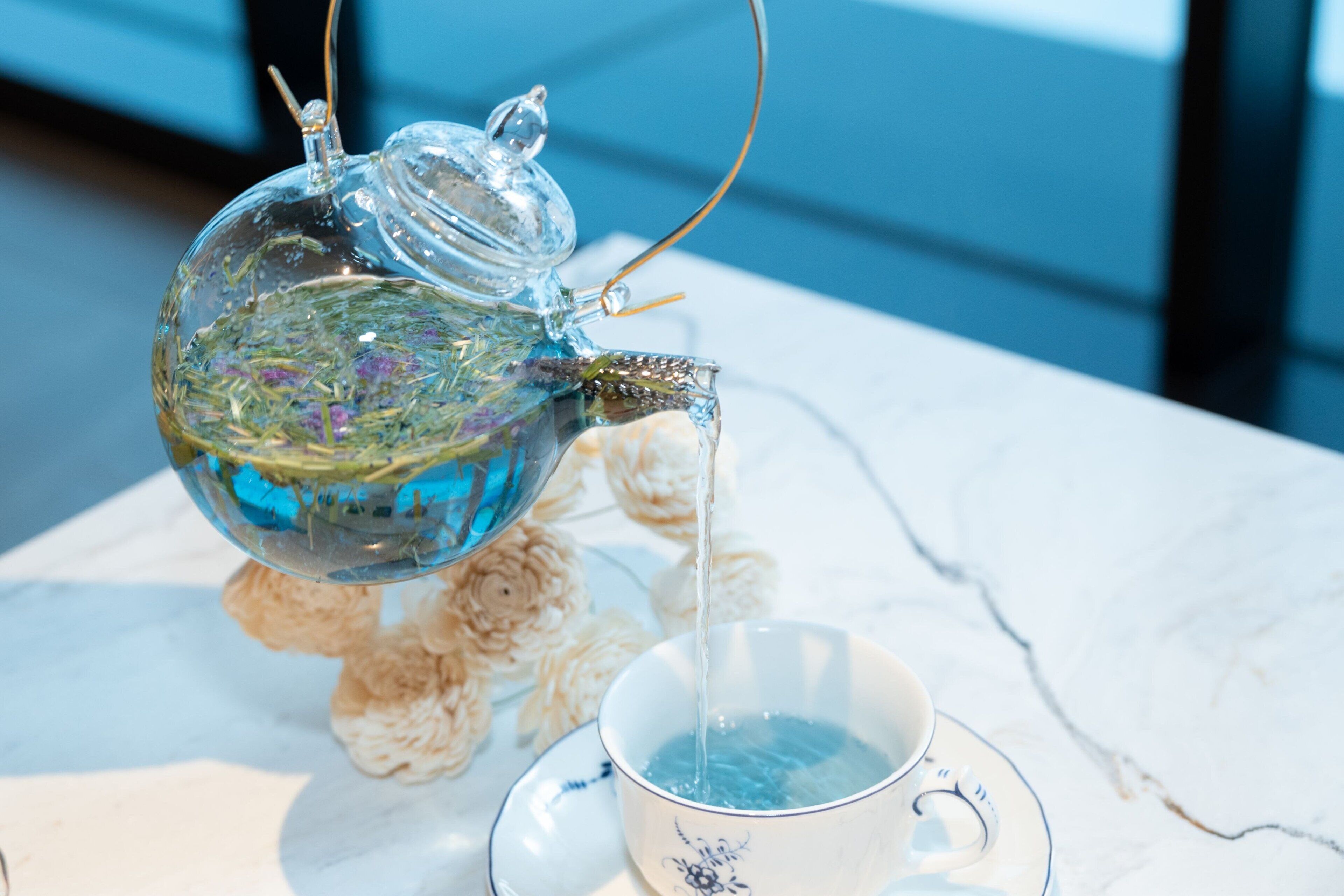 A clear glass teapot pouring water into a cup on a marble table.