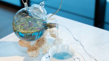 A clear glass teapot pouring water into a cup on a marble table.