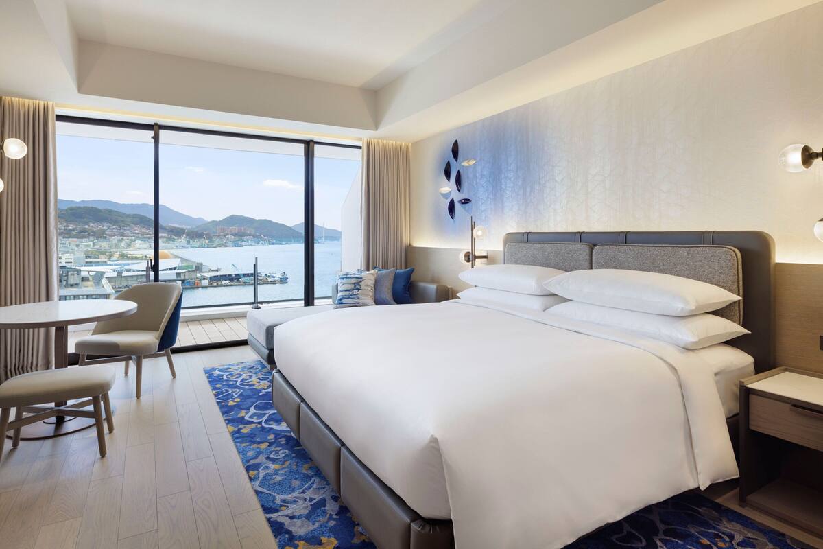 Hotelkamer met een groot bed, een bureau en een stoel. Door het raam is er uitzicht op een stad en bergen.
