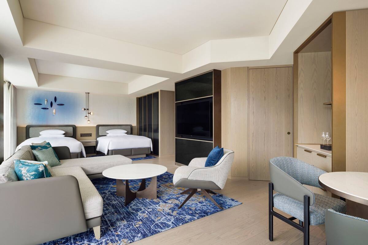 Een moderne hotelkamer met een groot bed, twee kleinere bedden, een bank, een eettafel en een televisie.