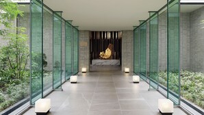 Un couloir moderne avec des panneaux de verre et un espace de détente central agrémenté d’une statue dorée.