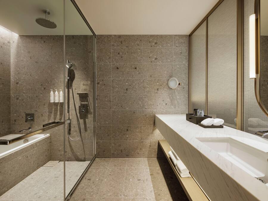 Un baño moderno con ducha de vidrio, un espejo grande y tocador con lavamanos y toallero.