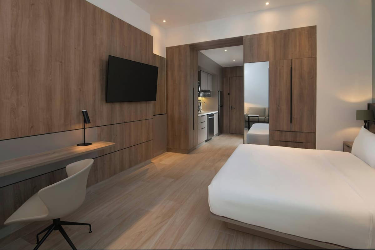 Une chambre d’hôtel moderne dotée d’un grand lit, d’un bureau avec une chaise, d’un téléviseur fixé au mur et de panneaux muraux en bois.