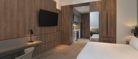 Una habitación de hotel moderna con una cama grande, un escritorio con una silla, un televisor montado en la pared y paneles de madera.