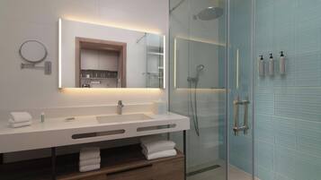 Un baño moderno con ducha envuelta en vidrio, tocador blanco con espejo y toallas dobladas con cuidado.