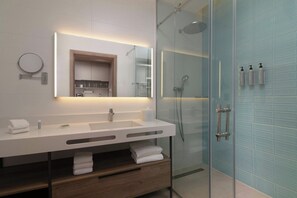 Un baño moderno con ducha envuelta en vidrio, tocador blanco con espejo y toallas dobladas con cuidado.