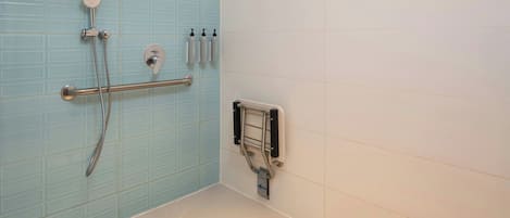 Un baño con pared de azulejos azules, ducha con cabezal de ducha manual, barra de apoyo y secador de manos.