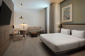 A modern hotel room with a large bed, a sofa, a small table, and a TV mounted on the wall.