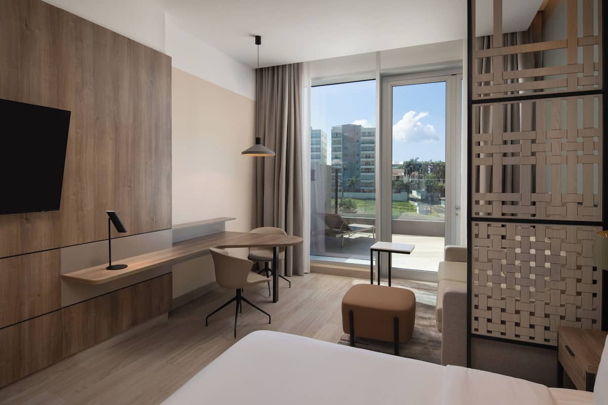 Une chambre d’hôtel moderne, dotée d’un grand lit, d’un bureau avec une chaise, d’une petite table et d’un téléviseur fixé au mur.
