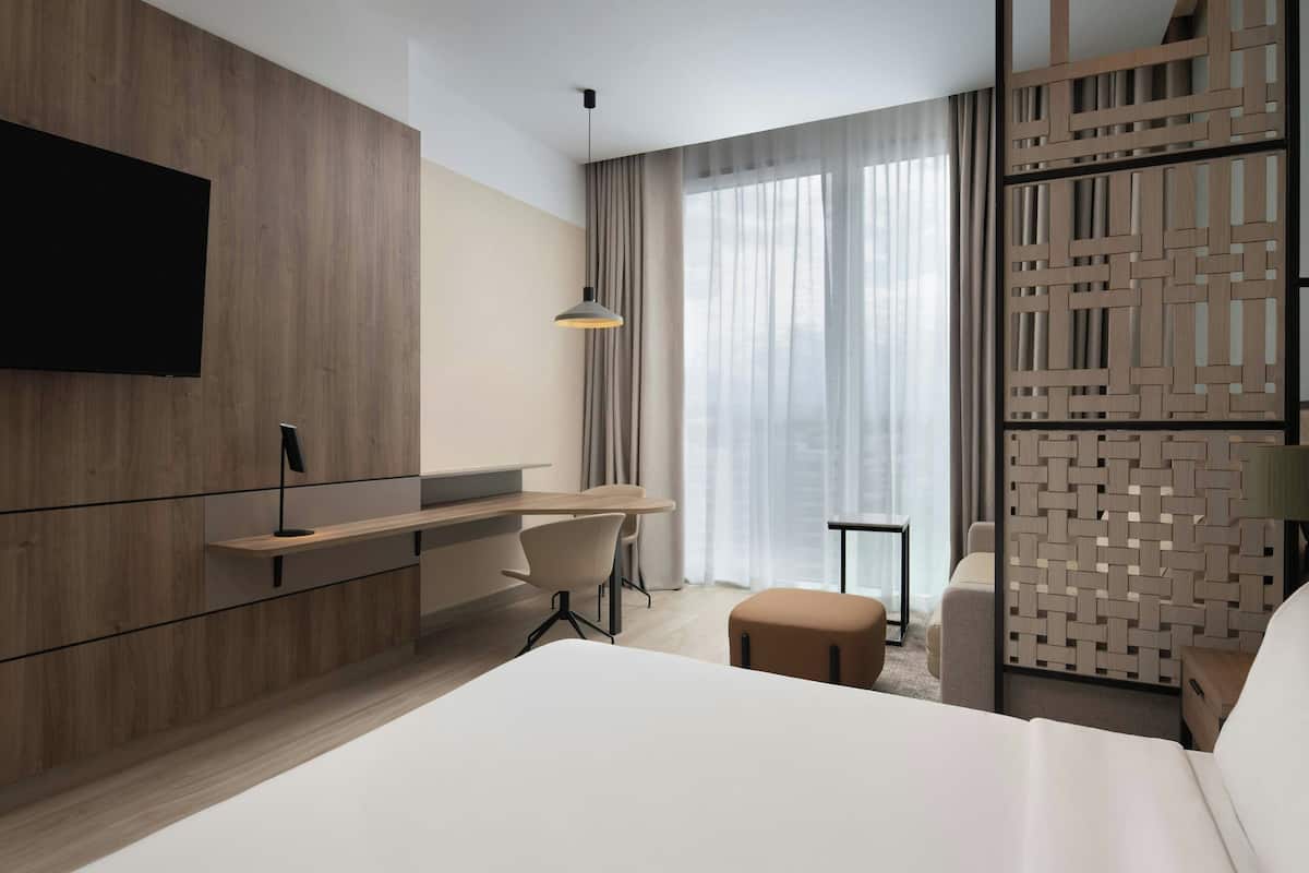 Une chambre d’hôtel moderne dotée d’un grand lit, d’un bureau avec une chaise, d’un téléviseur fixé au mur et d’une cloison décorative.