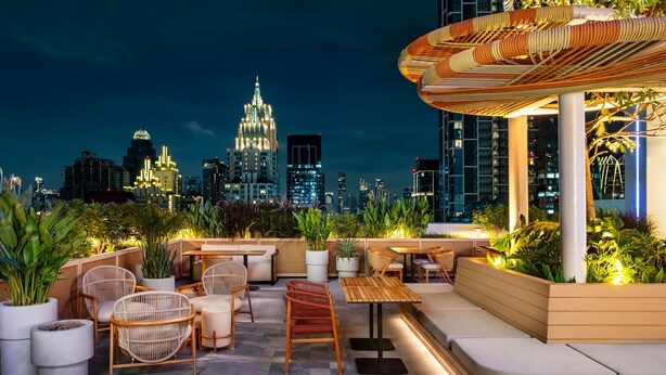 Una terrazza sul tetto con posti a sedere, piante in vaso e vista sullo skyline cittadino di notte.