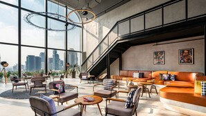 Un'area lounge moderna con posti a sedere, una scala e ampie finestre che offrono vista sulla città.
