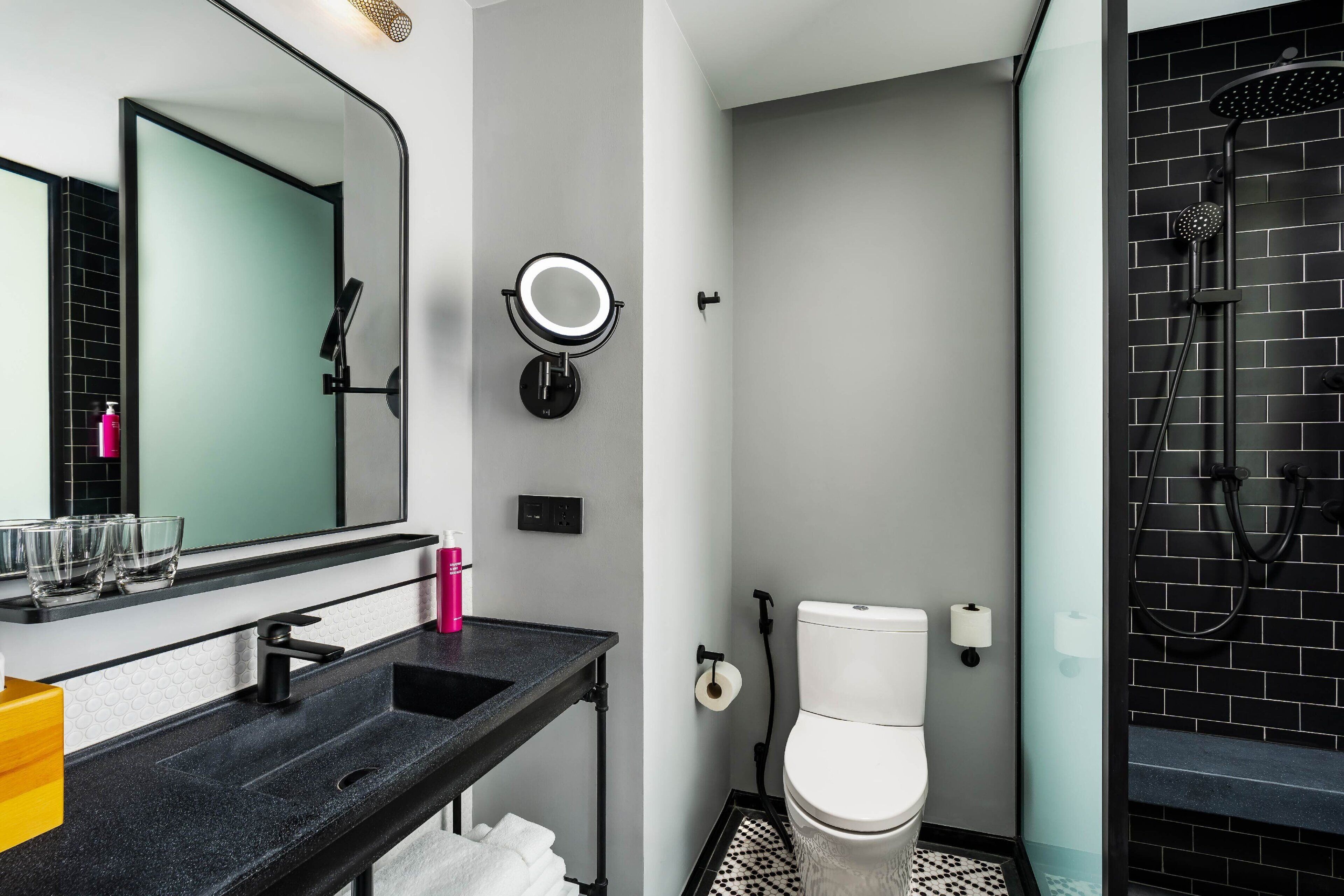 A modern bathroom with a black sink, a mirror, a toilet, and a shower area.