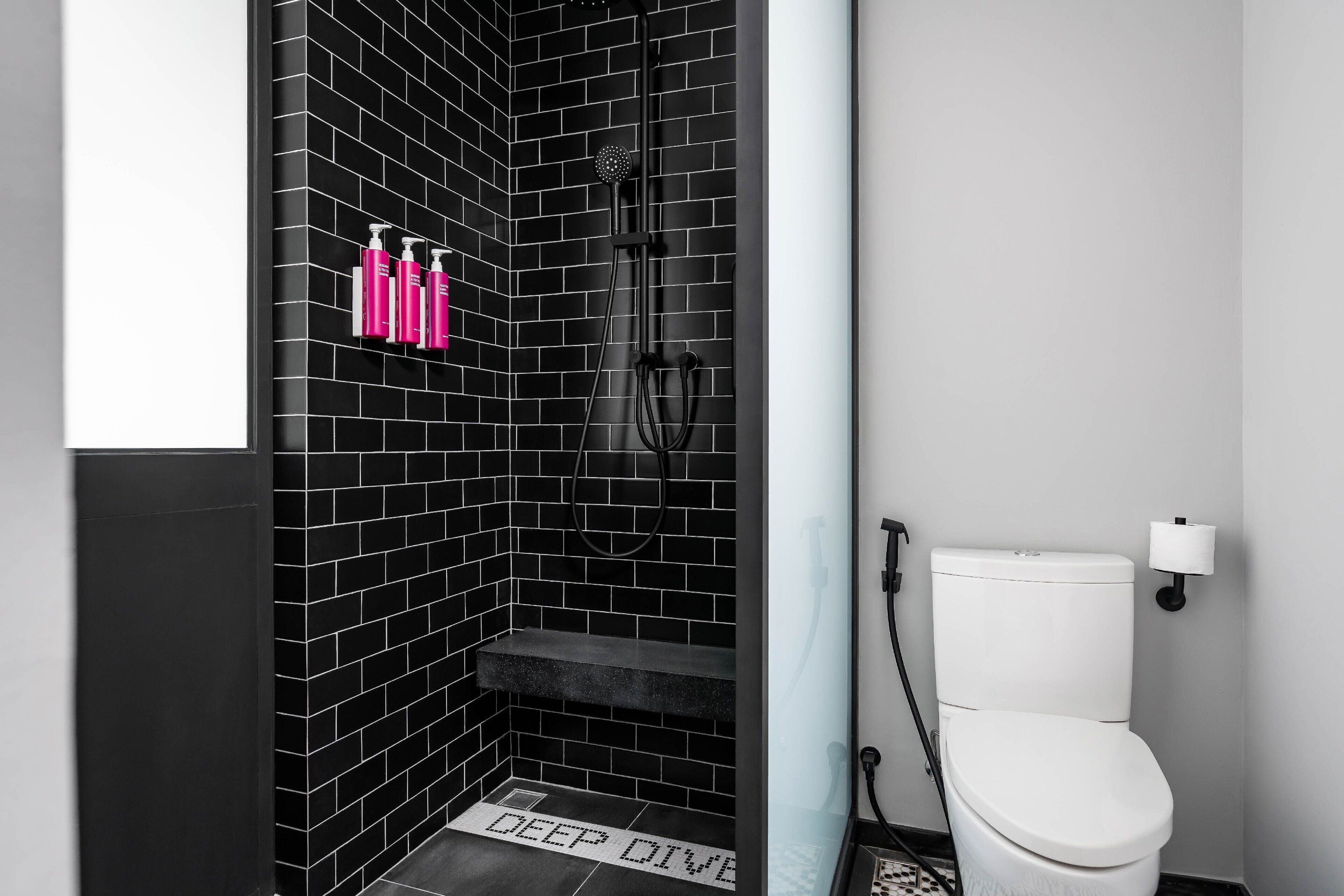 A bathroom with black tiled walls, a white toilet, and a shower area.