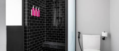 A bathroom with black tiled walls, a white toilet, and a shower area.